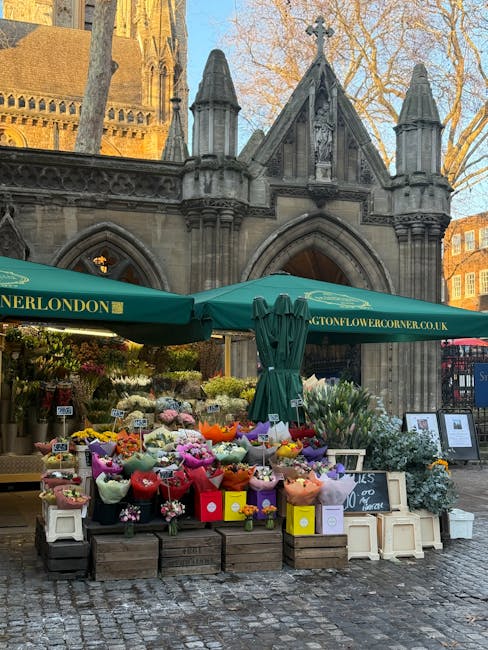 A floral arrangement display set up outdoors in front of a historic stone building with gothic architectural features. The display includes a variety of fresh flowers such as pink, yellow, purple, and