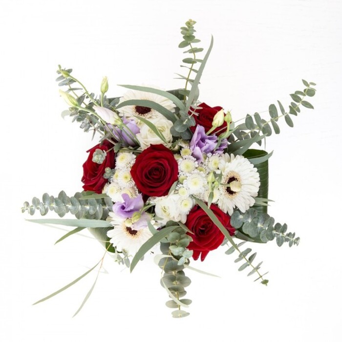 From the perspective of a Surrey Quays florist, this bouquet is an embodiment of balance and character-a creation that feels both classic and distinctly local. The white gerberas anchor the composition, petals splaying out around coffee-brown centres, offering brightness and a sense of calm confidence. Crimson red roses spiral alongside, their velvet blooms evoking lasting love and familiarity. The loose, flowing branches of eucalyptus lift the bouquet visually, casting delicate shadows across tables set for celebration or comfort-much like those seen in leafy corners of Russia Dock Woodland. Handfuls of soft, lilac-infused lisianthus peek through, adding a contemporary twist reminiscent of modern riverside living. Supporting all is a bed of rich, dark green foliage, their polished surfaces cupping the bouquet in a gentle embrace, united in a clear vase that showcases every verdant stem. There's an invitation here-to reach out, feel the textures, and breathe in the fragrance of rose, eucalyptus, and newly cut greens. Whether given as a gesture of love, sympathy, or gratitude, this elegant arrangement reflects the artistry and warmth of Surrey Quays, ready to elevate any home from Canada Water to the bustling docks.